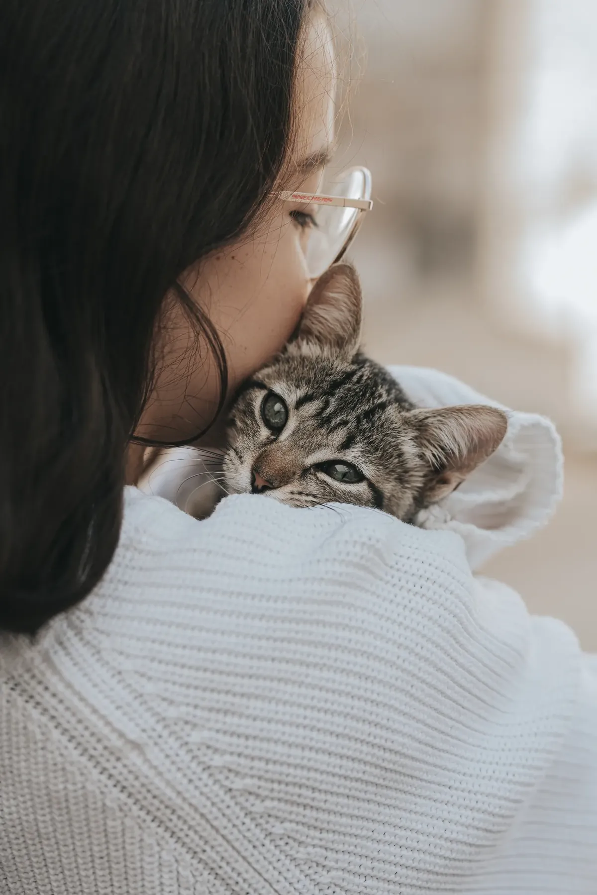 Woman holding a tabby kitten against her shoulder with her cheek pressed to its head