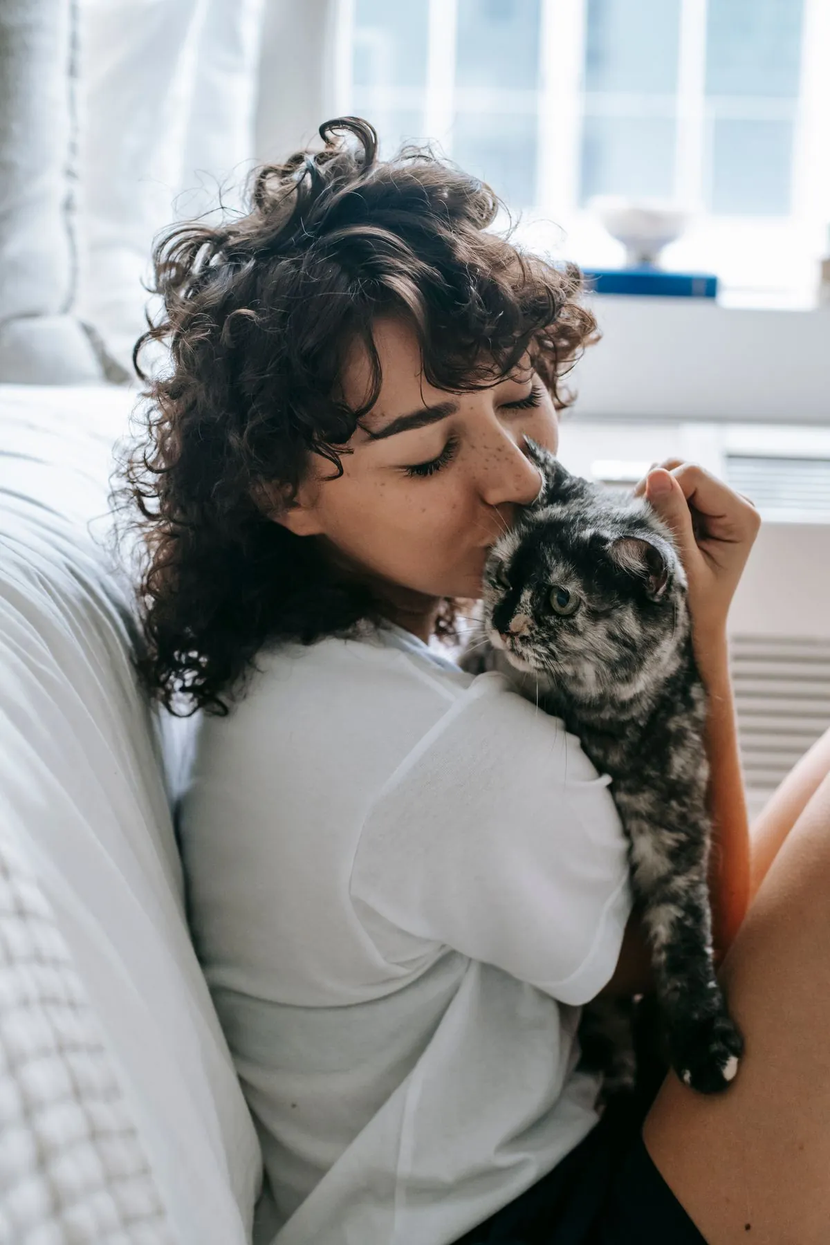 Woman relaxing on a sofa, affectionately holding her fluffy tabby cat