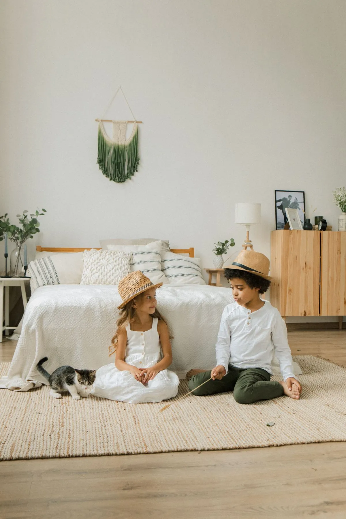 Two children in straw hats playing with a kitten on a rug