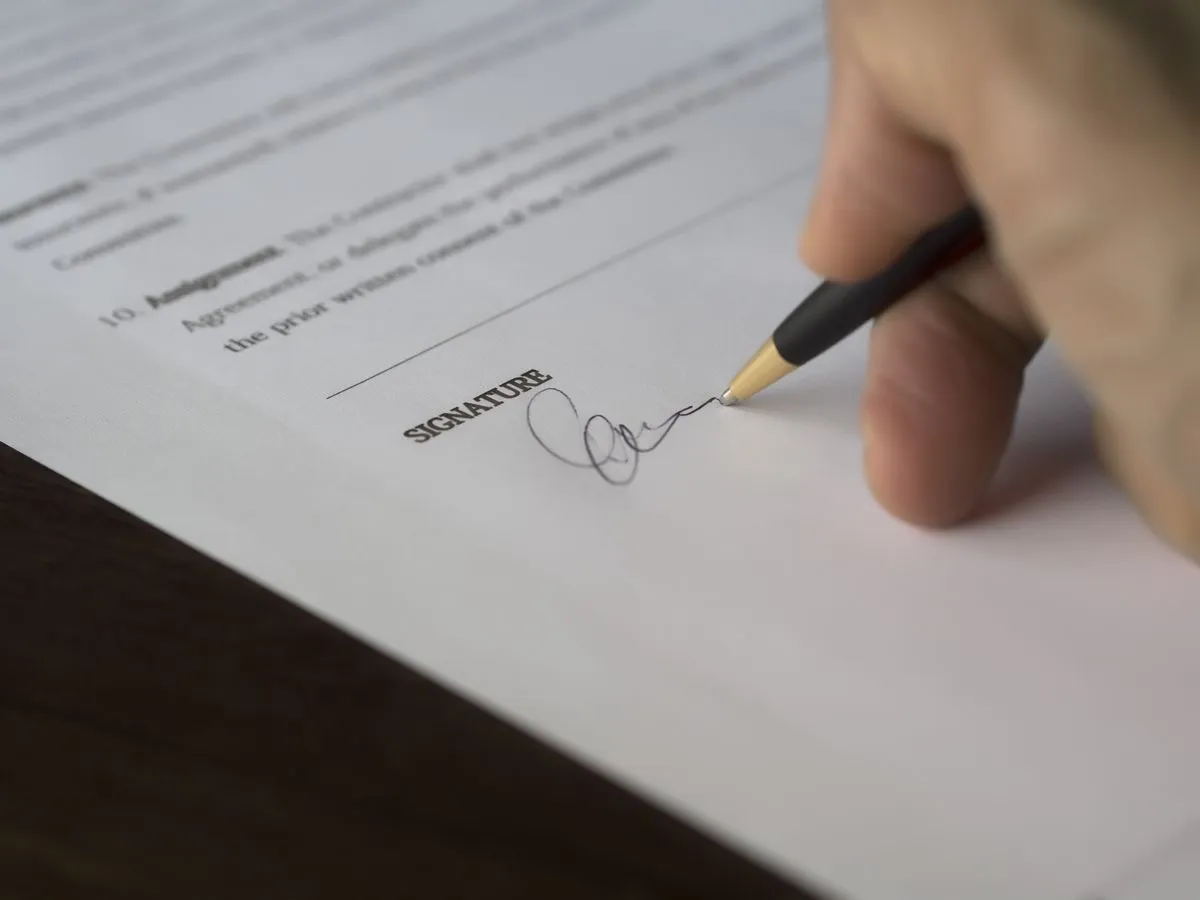 Hand signing a contract document with a pen on a desk