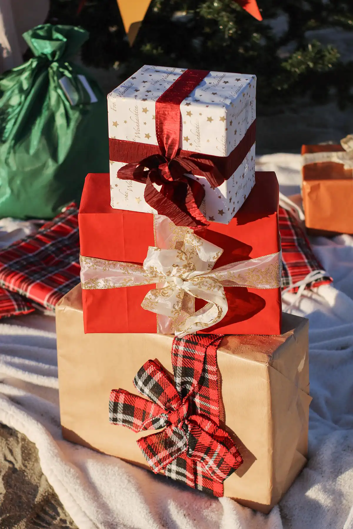 Wrapped presents stacked with wide fabric ribbons in red satin, sheer gold and plaid